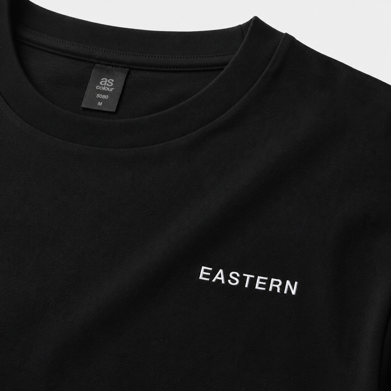 Close-up of EASTERN wordmark embroidery on Black Opening Round Tee