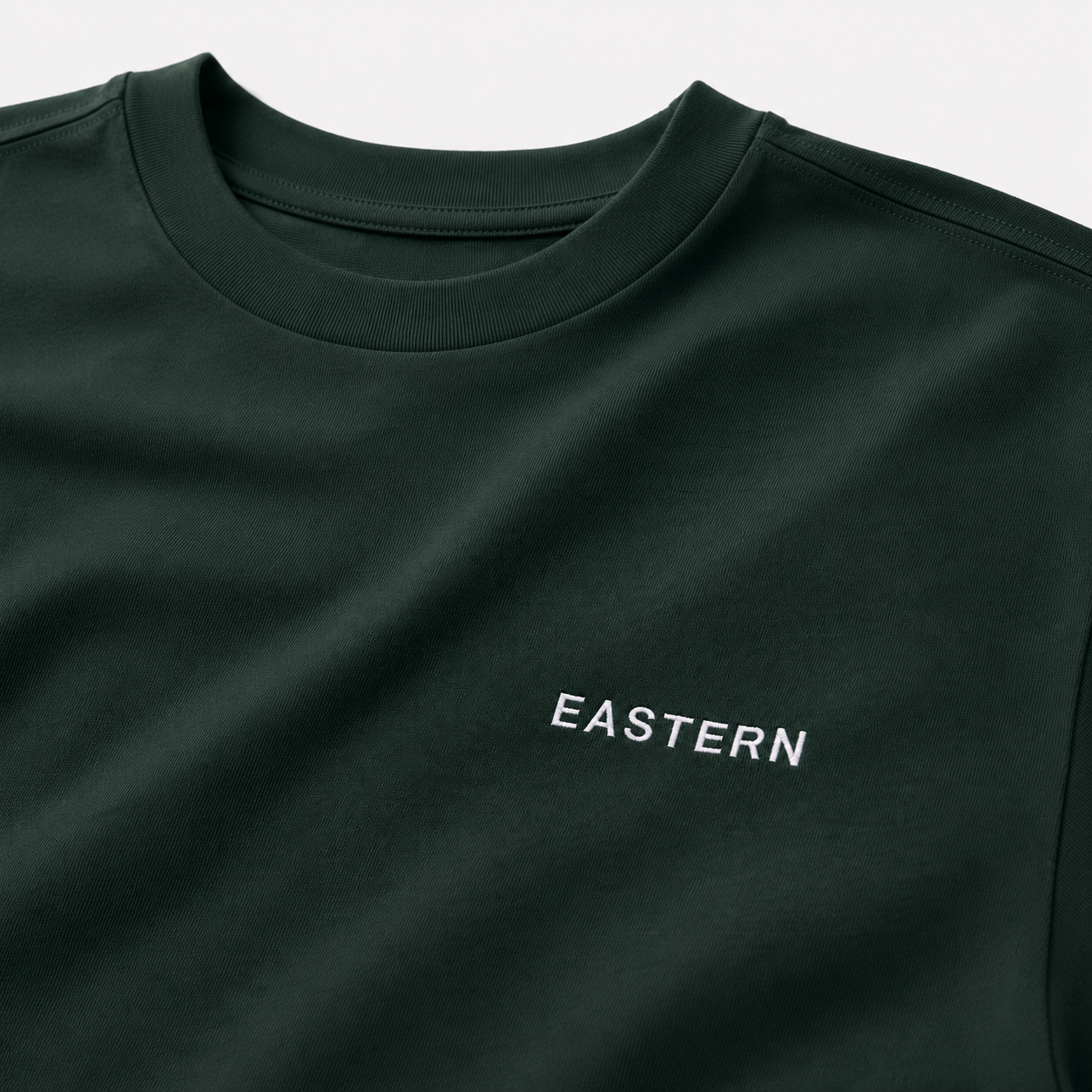 Close-up of EASTERN wordmark embroidery on Pine Green Opening Round Tee